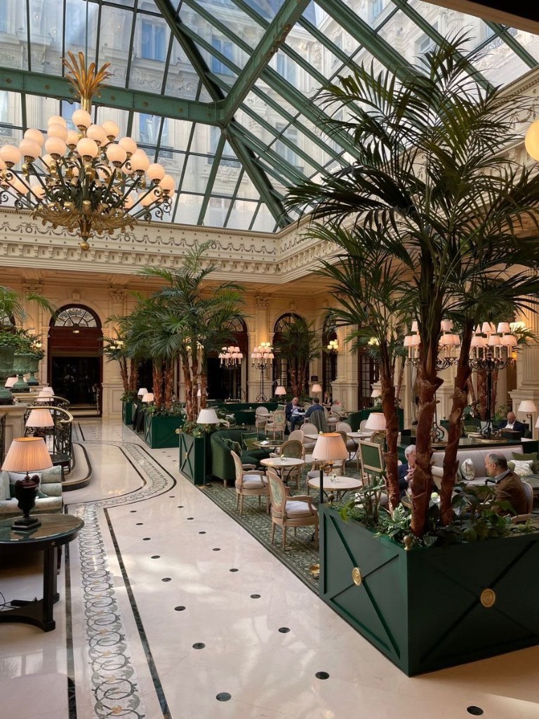 Lobby de hotel com claraboia, palmeiras e salão para chá
